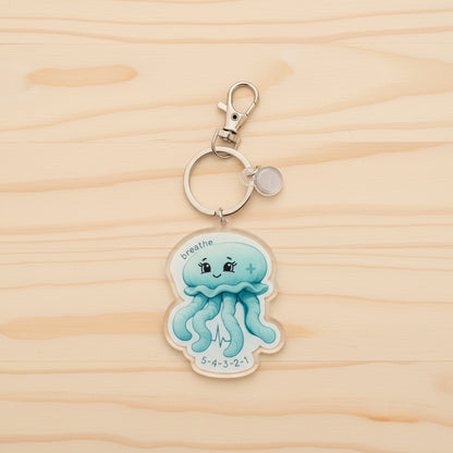 Keychain with a moon jellyfish design and 'breathe' text on a wood background